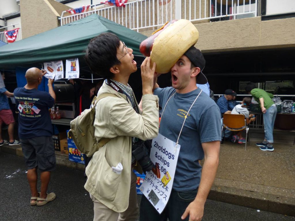 頭にホットドッグを載せている人がいたので、そのホットドッグを食べようとする奥村